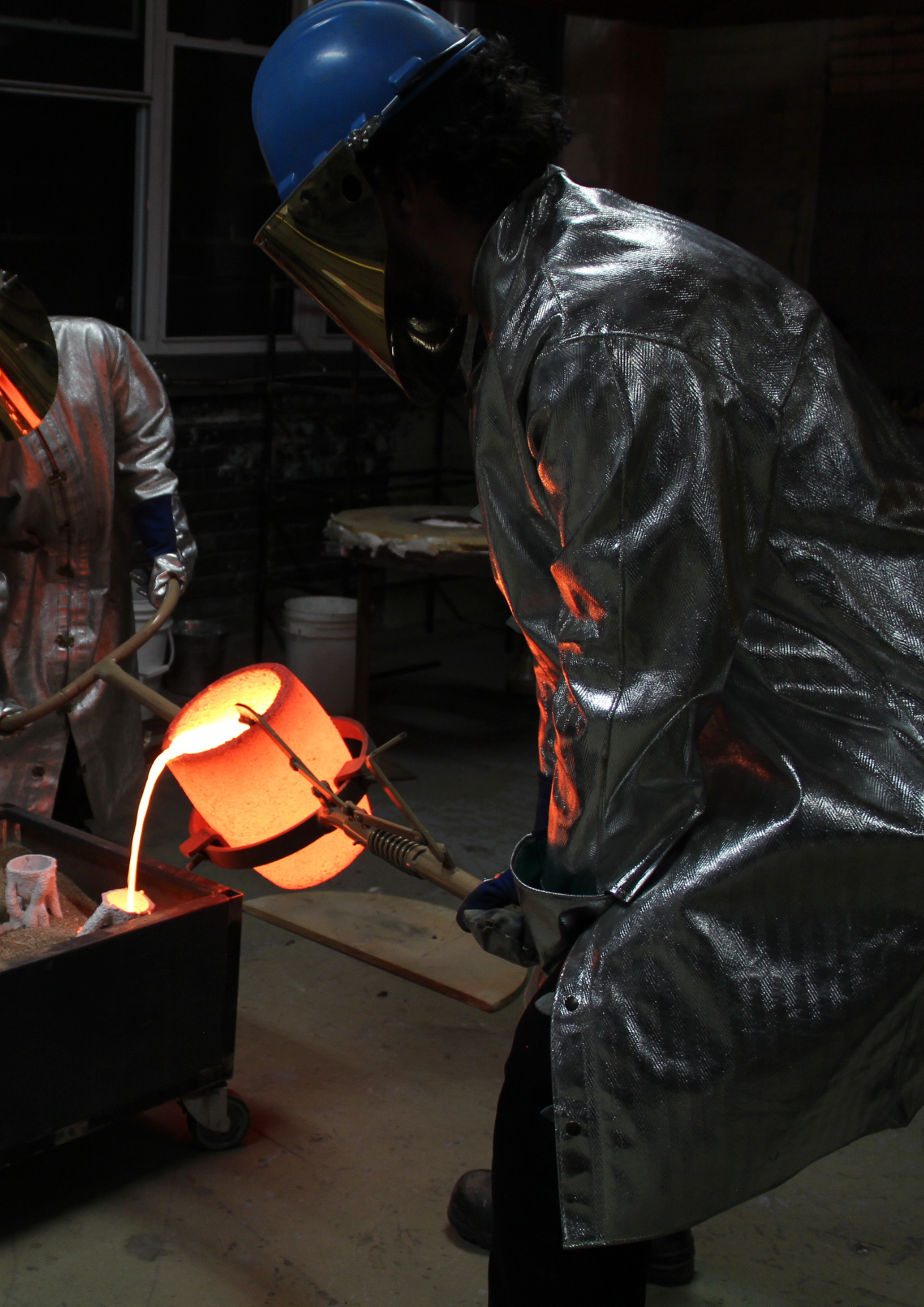 Deux fondeurs versent du bronze en fusion dans une moule